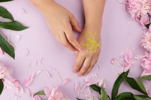 two female hands and thick green scrub and pink flowering peonies with green leaves, concept of anti-aging procedures for rejuvenating and moisturizing the skin of hands