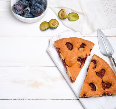 slices of biscuit plum cake on a white wooden board and fresh fruits, top view