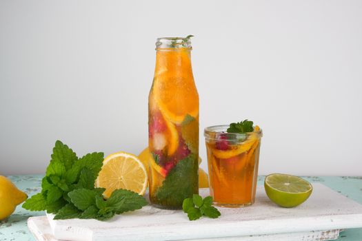 summer refreshing drink lemonade with lemons, cranberry, mint leaves, lime in a glass bottle, next to the ingredients for making a cocktail