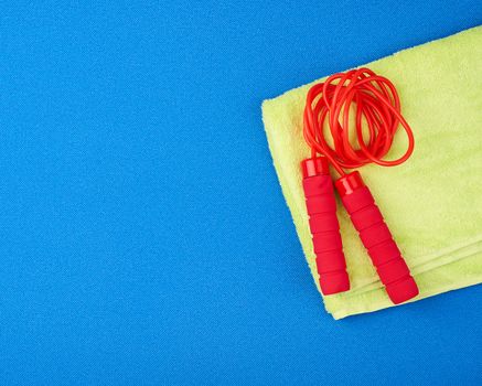 red jump rope lies on a neoprene blue sports mat and green towel, copy space