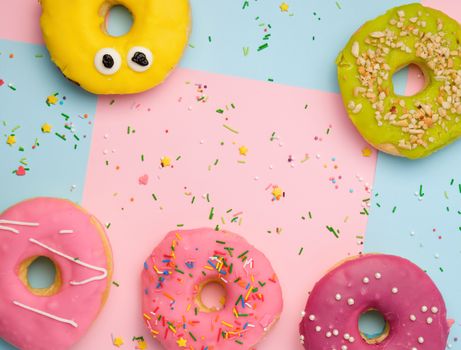 whole round pink donuts with colored sprinkles lie on a blue-pink background, top view, pastel colors