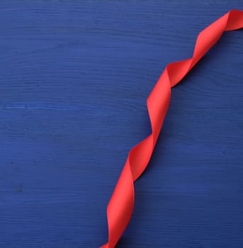 red silk thin ribbon twisted on a blue wooden background, trendy classic color, top view
