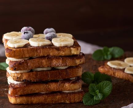 pile of square fried bread slices with chocolate and banana slices on a brown wooden board, French toast for breakfast
