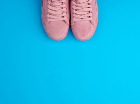 pair of sports pink sneakers with laces on a blue background, top view, place for text 