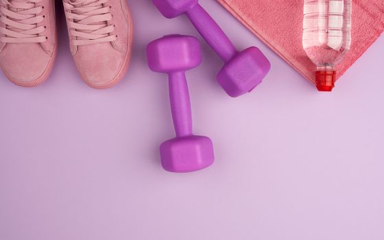 purple dumbbells and a clear plastic bottle of water, pink shoe on a terry towel, top view, flat lay, copy space