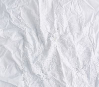 crumpled white cotton fabric with embroidery elements, fabric for sewing clothes and shirts, full frame