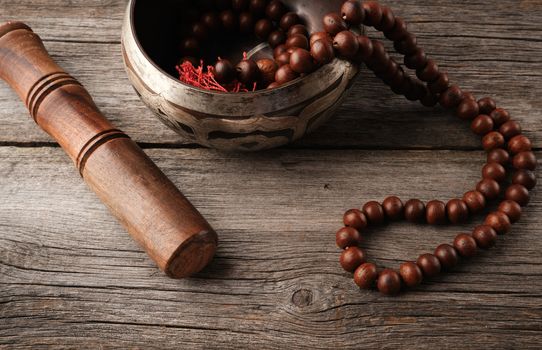 Tibetan singing copper bowl with a wooden clapper and prayer rosary on a gray wooden table, close up
