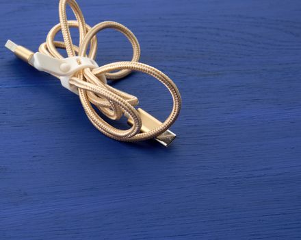 twisted golden cable for charging with electricity equipment in textile winding on a blue wooden background, close up