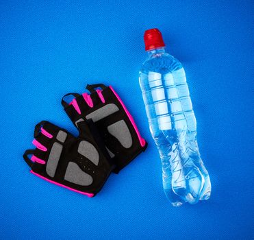 pair of sports gloves and a transparent bottle of water on a blue rug, top view