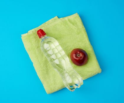 folded green terry towel and a transparent bottle of water on a blue background, concept of drinking more water while doing sports