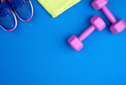 pair of purple plastic dumbbells, green terry towel, blue shoes on a neoprene mat, top view, training equipment, copy space