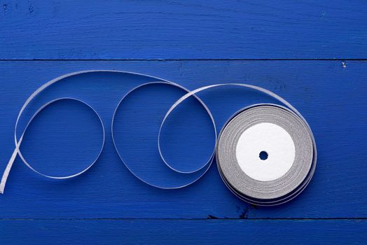 one round bobbin with silver ribbon on a blue wooden background, top view
