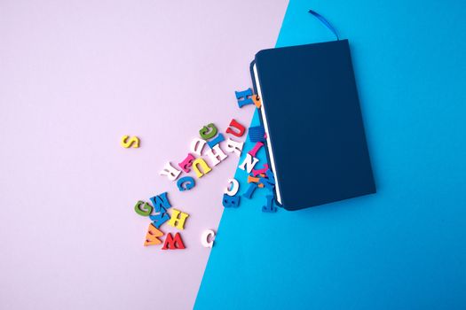 blue notebook and scattered wooden multi-colored letters on an abstract background, top view, flat lay