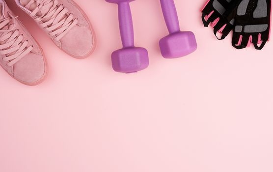 pair of pink leather sneakers, plastic dumbbells and gloves for sports on a pink background, sports backdrop, top view, copy space