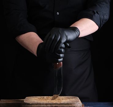 chef in a black shirt and black latex gloves holds a vintage kitchen knife for cutting meat, low key