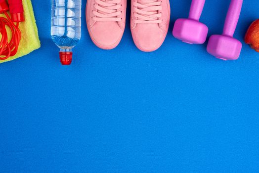 plastic purple dumbbells, sportswear, water, pink sneakers on a blue background from a sports mat, fitness kit, flat lay, copy space
