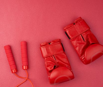 pair of red leather boxing gloves and red jump rope on a neoprene mat, sports set, top view
