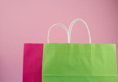 empty multicolored paper bags for shopping and gifts with white handles stand on a pink background