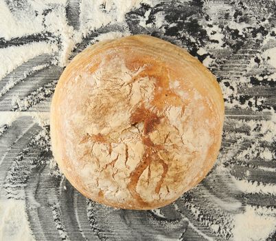 round baked bread and white wheat flour scattered on a black table, top view