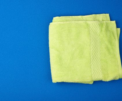 folded bath terry light green towel on a blue background, top view