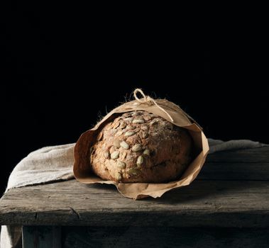 baked oval bread made from rye flour with pumpkin seeds, black background 