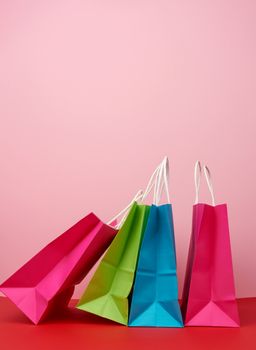 Four empty multicolored paper bags for shopping and gifts with white handles stand on a pink-red background, copy space