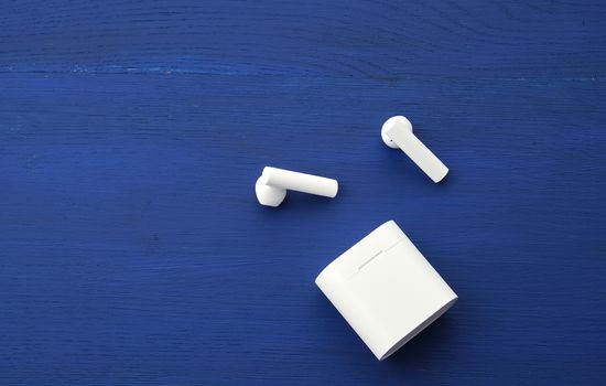 white wireless headphones and charging box on a blue wooden background, top view