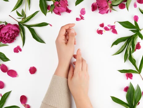 two hands of a young girl with smooth skin and a bouquet of red peonies on a white background, top view, flat lay