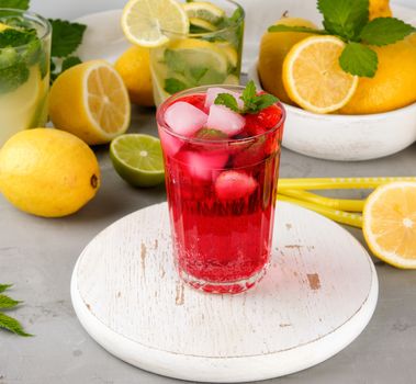refreshing summer drink of strawberrieson a white wooden board, behind it are yellow lemons and green mint leaves