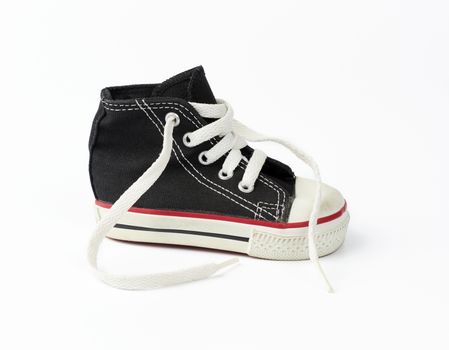 black textile children's sneaker with white untied shoelaces on a white background, shoes stand sideways