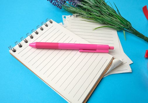 open notebook with white sheets and a pink plastic pen on a blue background, near a bouquet of flowers, close up