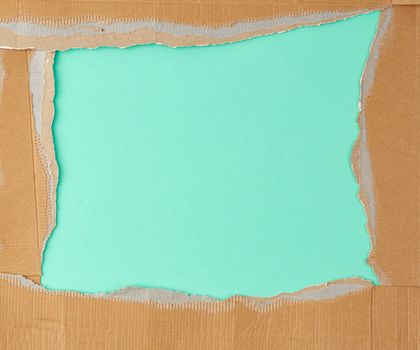torn edges of corrugated brown cardboard paper on a green background. Ripped paper texture