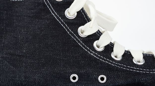 fragment of a black sneaker with white textile laces on a white background, close up