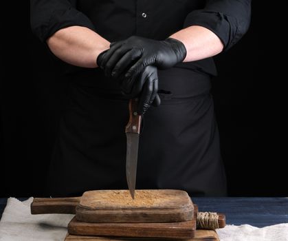 chef in a black shirt and black latex gloves holds a vintage kitchen knife for cutting meat, low key
