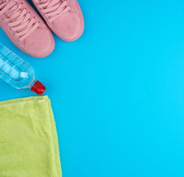 folded green terry towel and a transparent bottle of water, pink shoe on a blue background, concept of drinking more water while doing sports, copy space