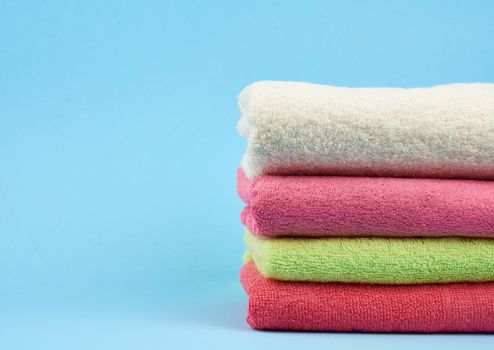 stack of colored cotton terry folded towels on a blue background, copy space
