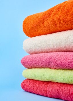 stack of colored cotton terry folded towels on a blue background, close up