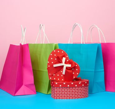 red paper box with a gift and paper bags for shopping stand on a pink-blue background