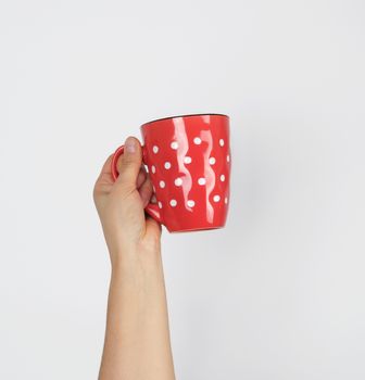 red ceramic cup in a female hand on a white background, hand is raised up