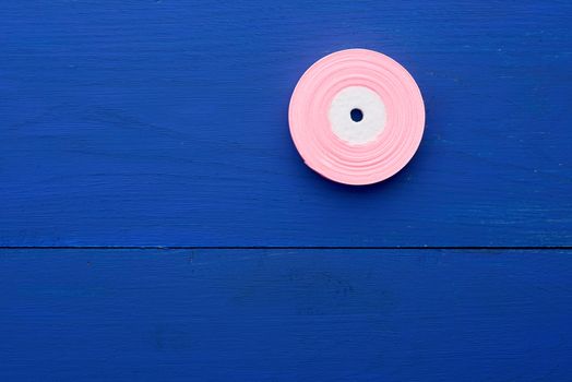 one round bobbin with pink ribbon on a blue wooden background, copy space