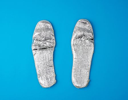 pair of shoe insoles with insulation and foil on a blue background, top view