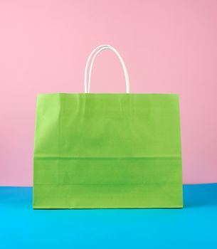 empty green paper bag with white handles for shopping and gifts on blue pink background