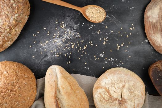 baked various loaves of bread on a black background, top view