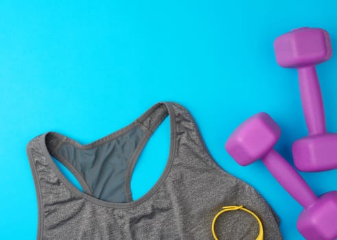 pair of purple plastic dumbbells, gray sports shirt on a blue background, set for sports, flat lay