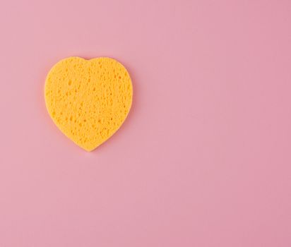 yellow heart shaped sponge for face wash on pink background, copy space