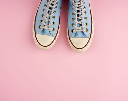 pair of old worn blue sneakers with white laces on a pink background, top view