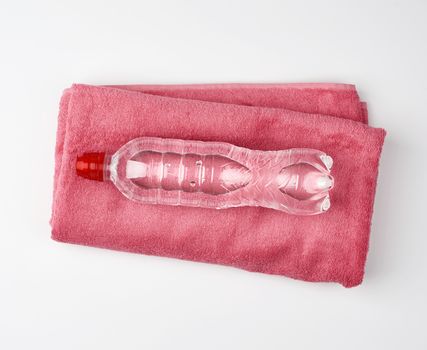 folded pink terry towel and a transparent bottle of water on a white background, concept of drinking more water while doing sports