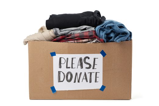 large brown cardboard box with the inscription please donate, box is filled with various clothes and is isolated on a white background
