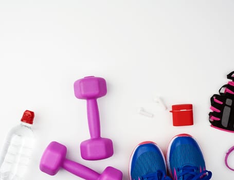 plastic purple dumbbells, bottle of water, blue sneakers and wireless headphones on a white background, fitness kit, flat lay, copy space