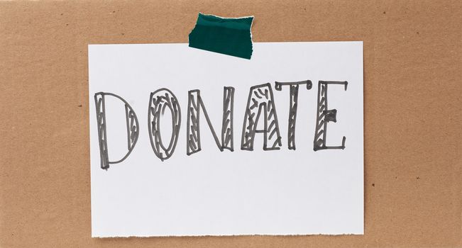 inscription donate on a white sheet and glued brown cardboard paper, concept of volunteering and promotion